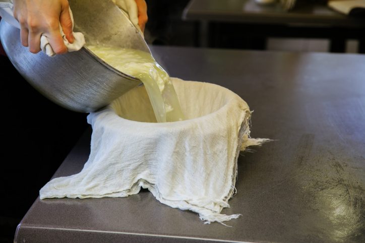 Pouring paneer cheese into cheesecloth.