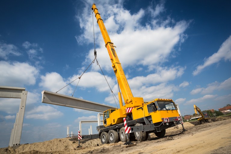 Bright yellow ASME B30.5-2021 mobile crane lifting in action under blue sky.