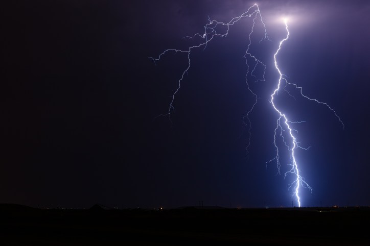 A blue bolt of lightning strikes the ground beneath a dark sky in an act of electrostatic discharge.