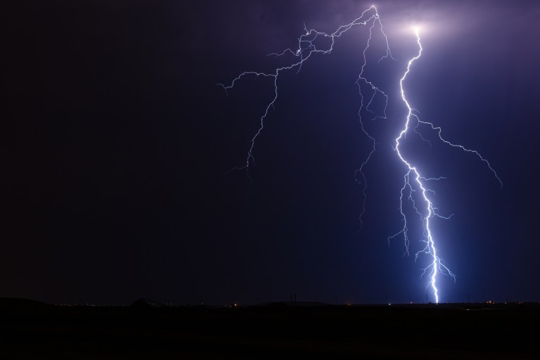 A blue bolt of lightning strikes the ground beneath a dark sky in an act of electrostatic discharge.