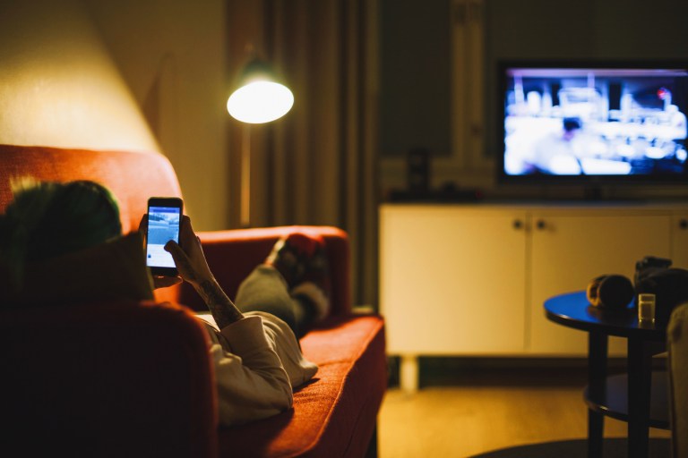 Woman lying on couch with phone while watching TV on electronics assessed to EPEAT certification.