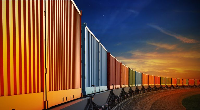 Railroad lineup of colorful ASTM D4169-22 performance-tested shipping containers under sunset.