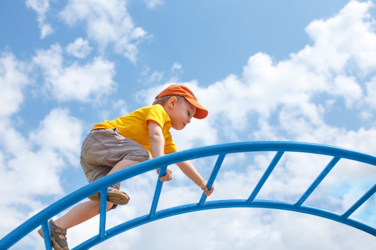 Boy climbing monkey bars under sky in playground kept safe with ASTM F1148.