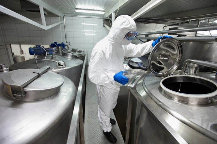 Lab specialist opening vat in hazmat suit to fix nonconformity through corrective action and preventative action.