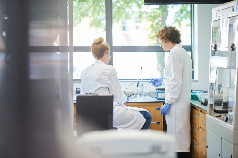 Geneticists working in ANSI/ASSP Z9.5-2022 ventilated lab in front of tree filled window.