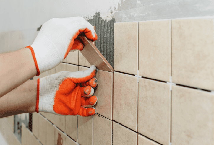 Orange gloves following ANSI A108/A118/A136.1:2024 to lay ceramic tile.