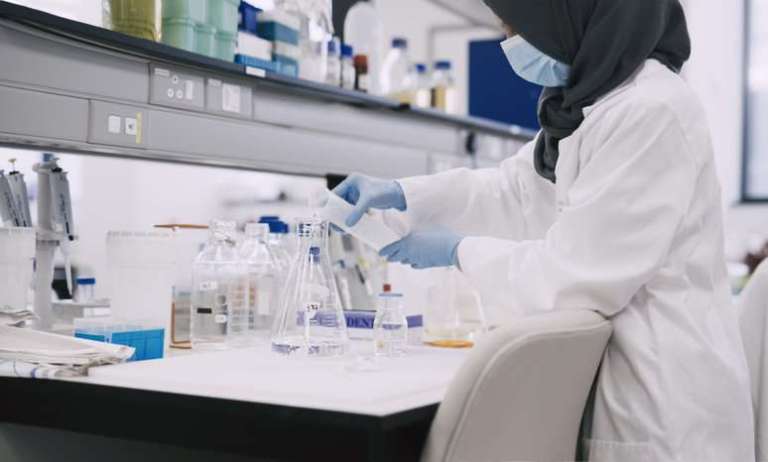 Female scientist pouring chemical into beaker before preparing reference material and certified reference material.