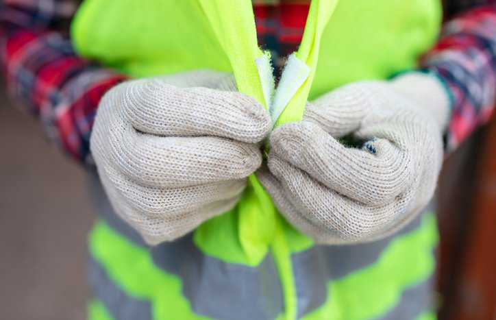 Closeup of worker donning green high visibility safety apparel (HVSA) vest designed to ANSI/ISEA 107.