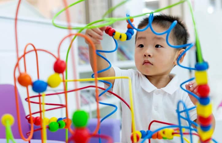 Little boy working on colorful toy puzzle safely with ISO 8124-1:2022 requirements.