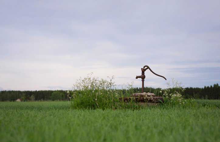Water well pump in a grassy field that is protecting with state regulations and CDC and EPA recommendations.