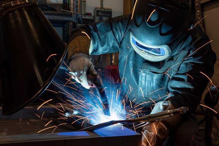 Welder Wearing Safety and Health Equipment Adhering to ANSI Z49.1-2021.
