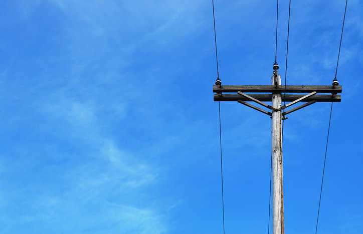 Wood utility pole, under ANSI O5.1-2022, beneath blue sky