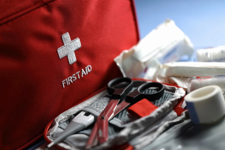 A red workplace first aid kit filled with the proper ANSI Z308.1-2021 standard contents.
