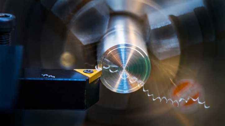 Operator using a lathe, adhering to machine safety in ANSI B11.6-2022.