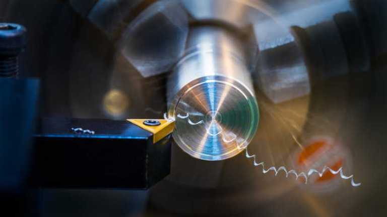 Operator using a lathe, adhering to machine safety in ANSI B11.6-2022.