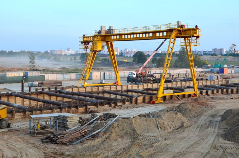 An overhead gantry crane operating at an outdoor construction site that is lifting a heavy load; the crane is adhering to ASME B30.2‑2022 standard's safety requirements.