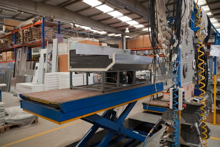 Blue ANSI MH29.1 scissor lift table raising metal in warehouse or factory.