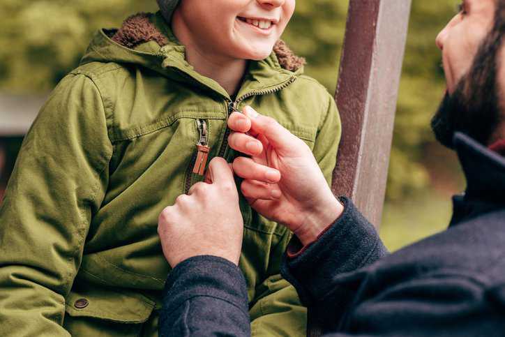 Father putting on his child's jacket that adheres to safety specifications in ASTM F1816-18.