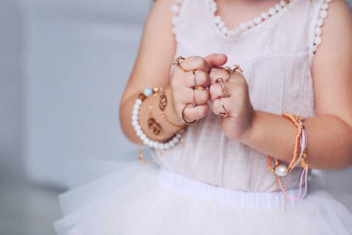 Baby girl adorned in jewelry like rings and bracelets that adhere to ASTM F2923-20.