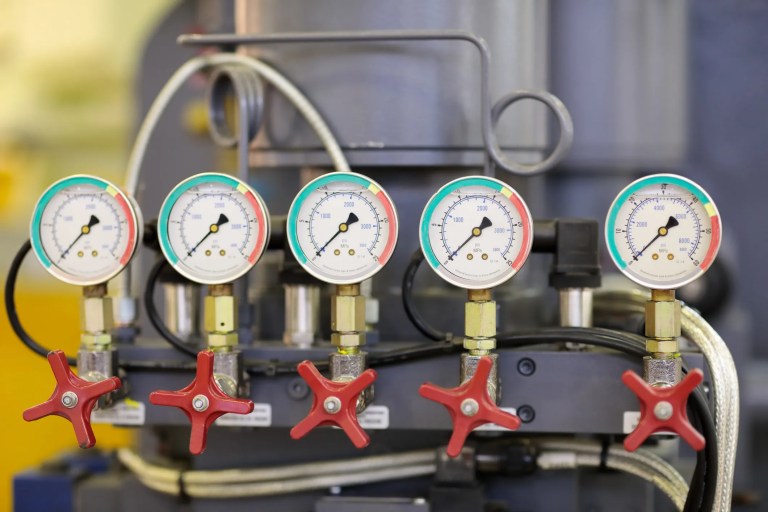 Close-up of a ASME B40.100 compliant pressure gauge mounted on industrial piping, displaying precise pressure readings with metal valves and machinery in the background, highlighting safety and accuracy in a manufacturing environment
