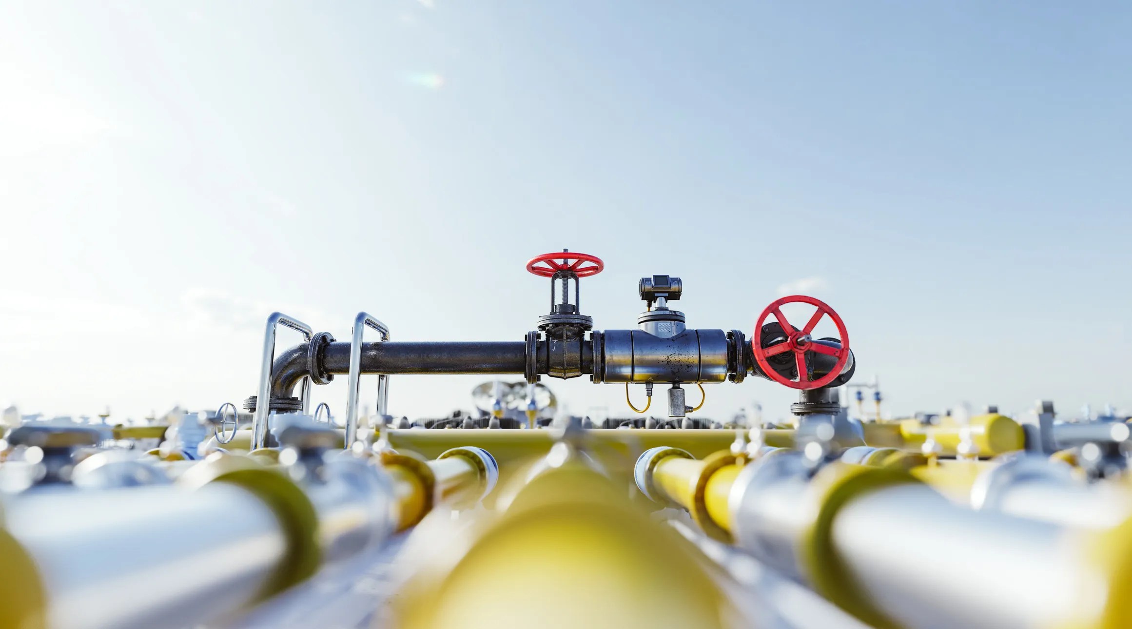 A wide-angle photo of a natural gas transmission pipeline in a field or facility, with visible pipe segments, valves, and signage.