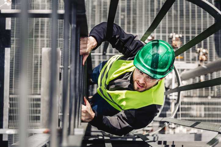 Man climbing a caged ladder while donning ANSI/ISEA 107-2020 High-Visibility Safety Apparel.