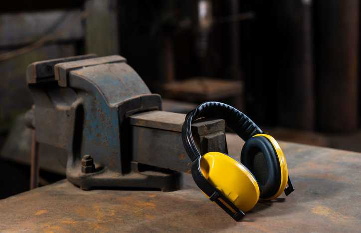 Yellow ear protection sitting on rusty workbench that leads to high workplace noise hazards.