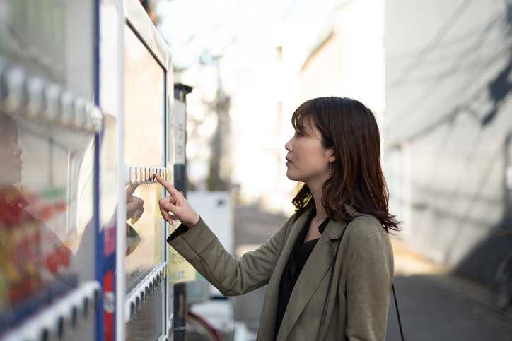 Woman pushing button on NSF/ANSI 25-2022 vending machine on Japanese street.