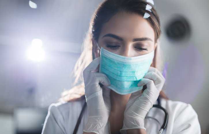 Young female doctor wearing medical face mask adhering to ASTM F2100-23 before surgery.