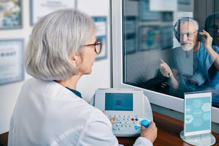 Patient getting pure tone hearing test at audiology center with an audiometer adhering to specifications in ASA/ANSI S3.6-2018 (R2023).