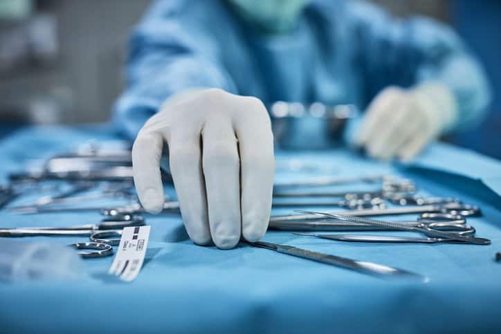 Surgeon in health care facility picking up medical devices that adhere to risk management requirements in ISO 14971:2019.