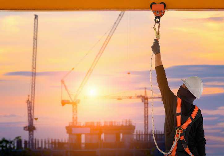 Construction worker adhering to ANSI/ASSP A10.32-2023 fall protection and fall prevention requirements.