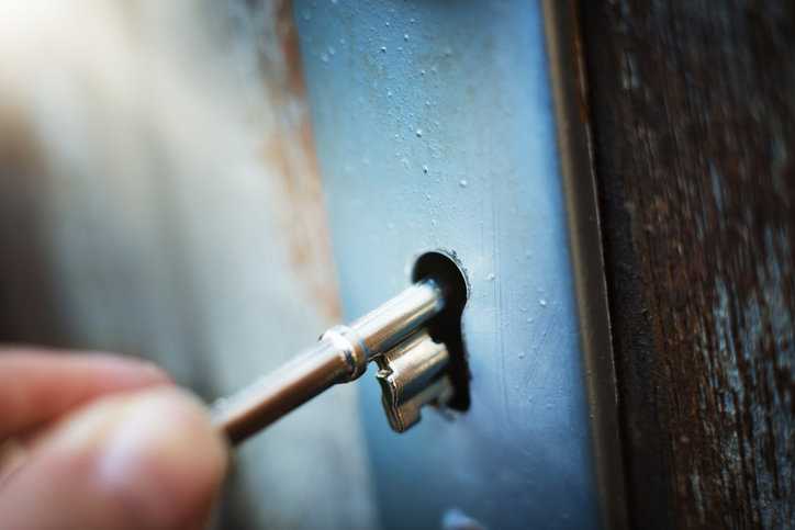 Shiny key inserting into blue mortise lock under ANSI/BHMA A156.13-2022.
