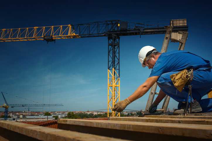 Closeup side view of a construction worker preparing wooden scaffolding protected by ANSI/ASSE Z359.