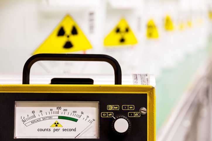 Geiger counter with radioactive materials in the background adhering to ASTM D3648-23 practices for measurement of radioactivity.
