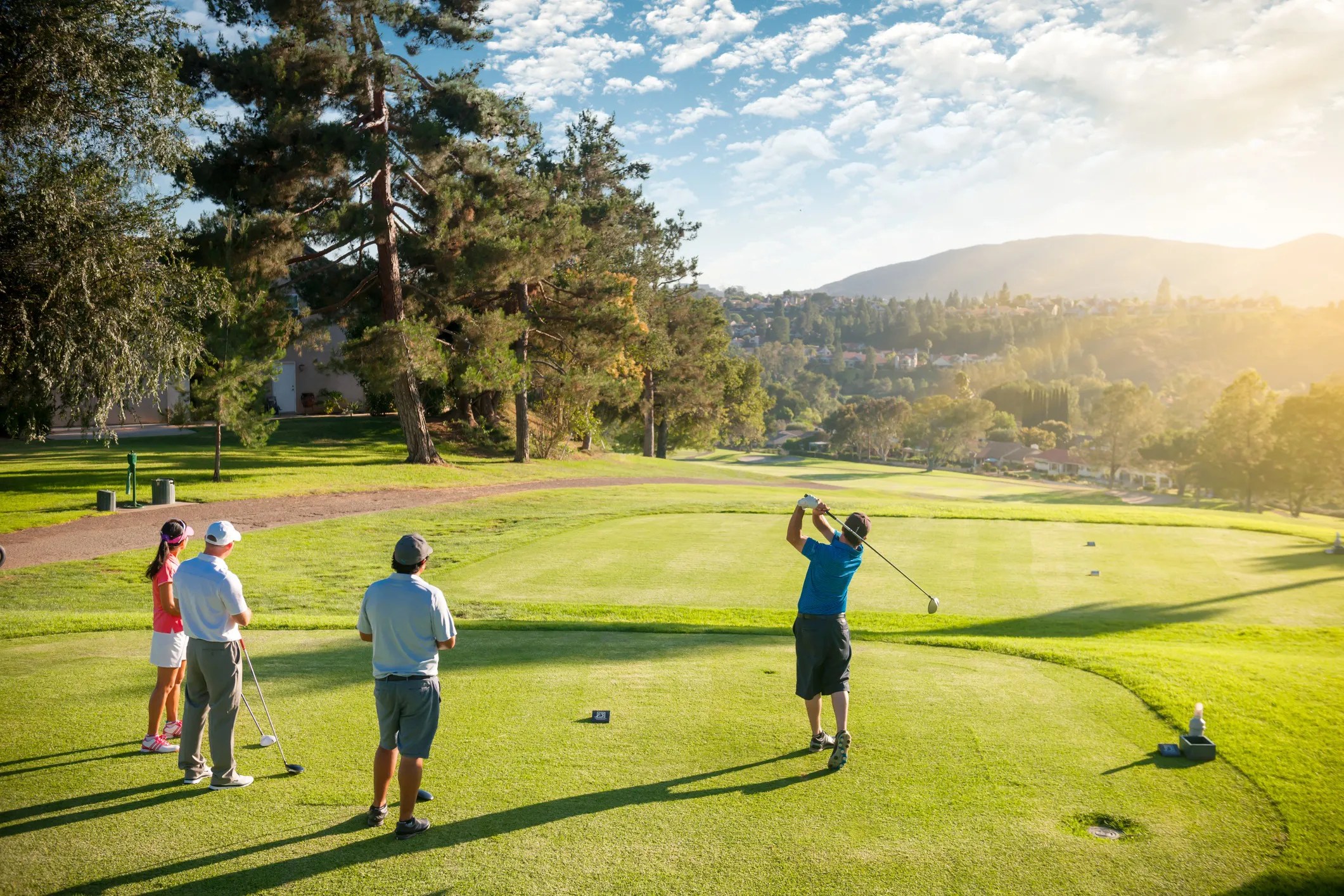 A man teeing off as his friends on a beautiful, sunny day at the golf course.