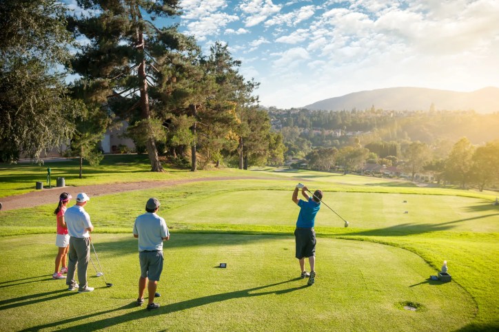 A man teeing off as his friends on a beautiful, sunny day at the golf course.