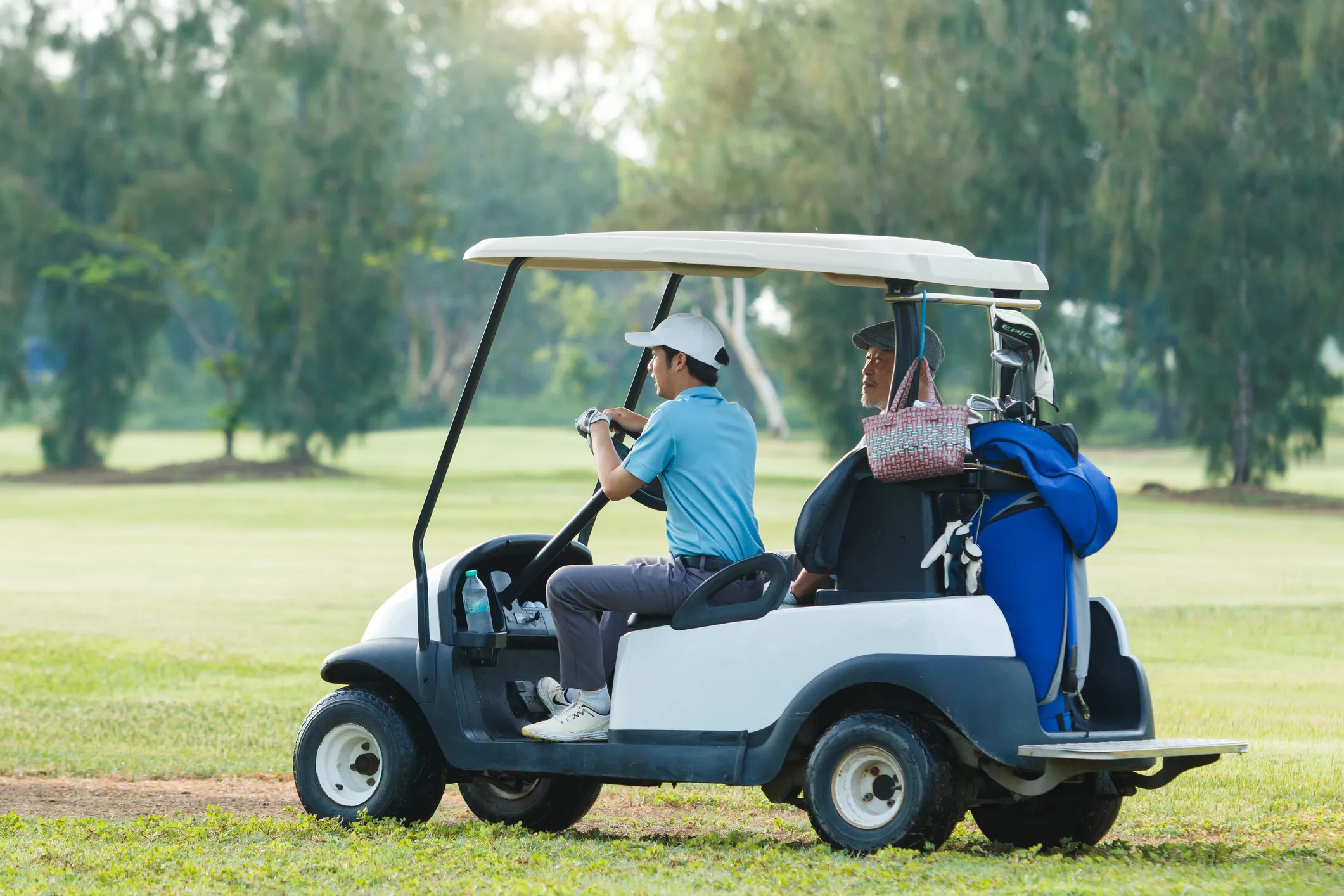 Father and son driving a golf car on a green, lush golf course adhering to ANSI/OPEI Z130.1-2020 requirements. 