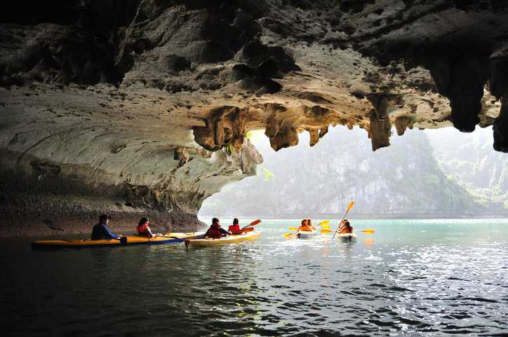 Travelers kayaking under a cave in the ocean, partaking in adventure tourism.