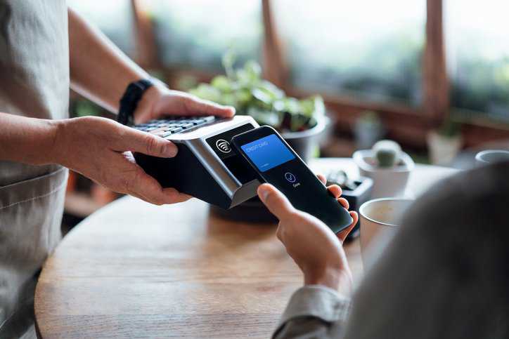 A man paying bill with credit card contactless payment on smartphone in a café and hence the secure financial card transaction message is adhering to ISO 8583:2023.