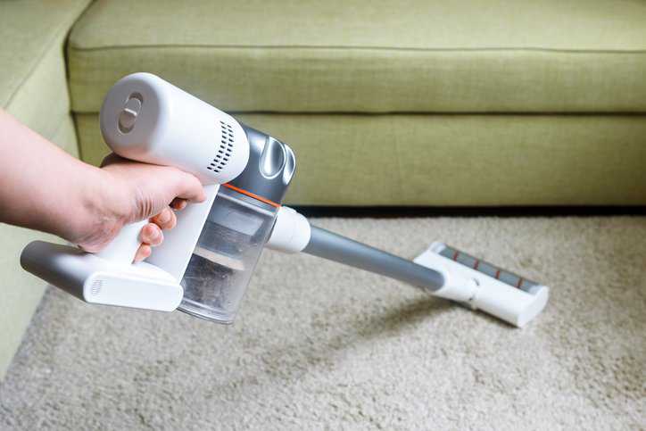 Wireless vacuum cleaner with HEPA filter, adhering to ASTM F1977-22, used on carpet in living room.