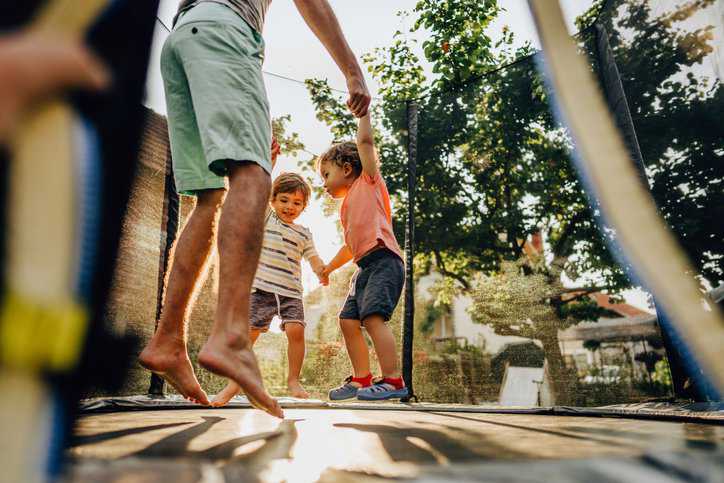Father and his boys having fun jumping on the trampoline that adheres to consumer safety guidelines in ASTM F381-16.