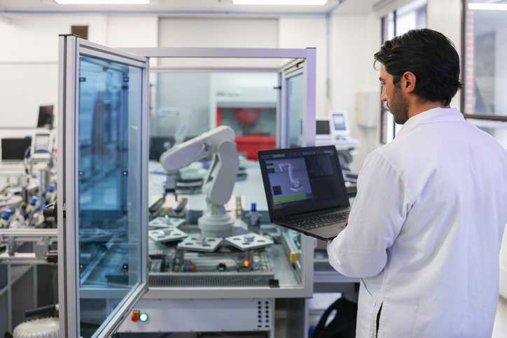 Researcher at engineering lab developing a robotic arm using a laptop computer that adheres to ASTM E1578-18 laboratory informatics.