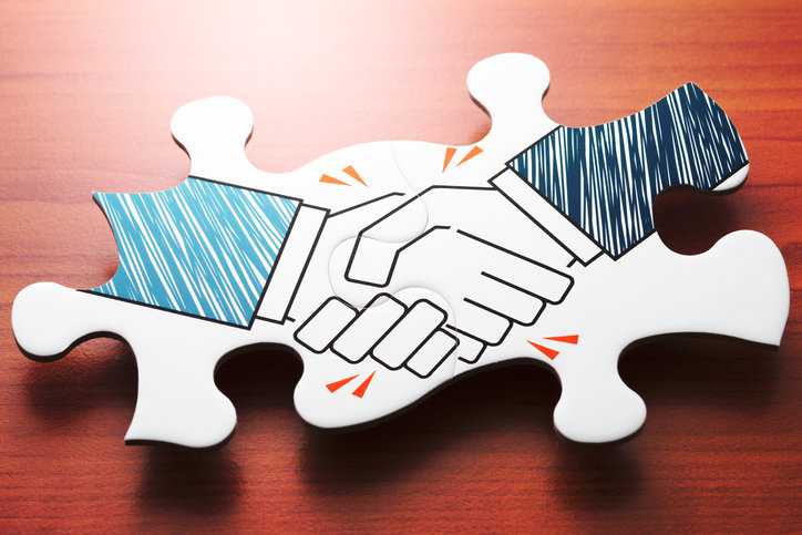Hand shaking on wooden jigsaw piece showing the demonstration of conformity assessment requirements.
