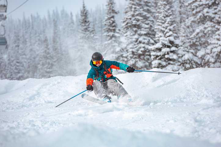 Alpine skier rides over off-piste slope in snow capped forest with ski-bindings adhering to ISO 9462:2023.
