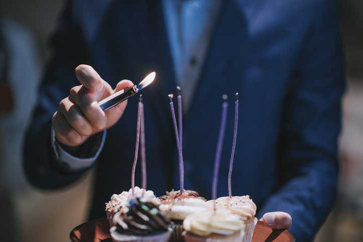 A man using a utility lighter, adhering to ASTM F2201-20, to light cupcakes for a surprise office birthday celebration.
