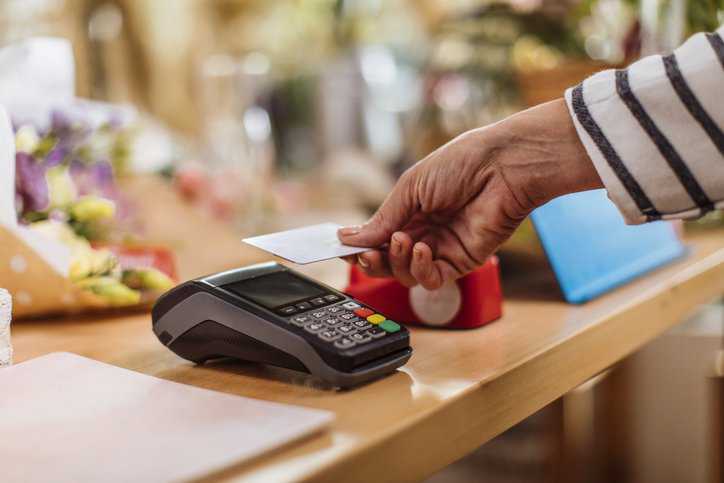 A woman making a contactless credit card payment at the flower shop with her integrated circuit card adhering to ISO/IEC 7816-4:2020.