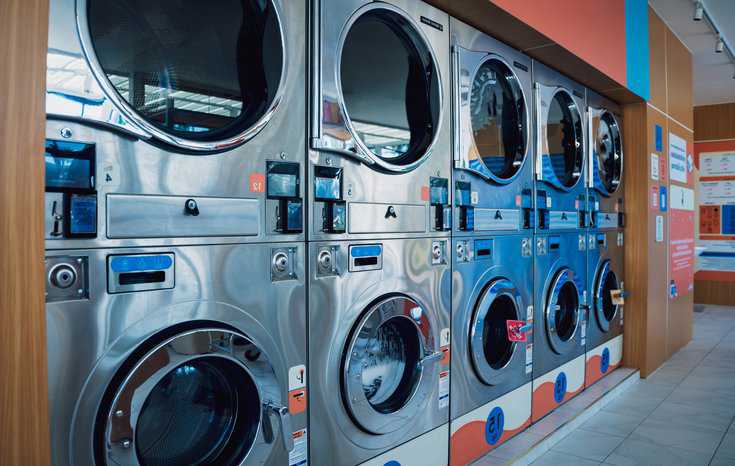 Rows of industrial laundry machines in the large laundromat with clothing dryers adhering to ANSI Z21.5.2-2016/CSA 7.2-2016.