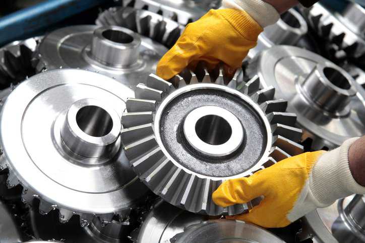 An engineer working on a gear and wheel and is wearing hand protection adhering to ANSI/ISEA 105-2016.