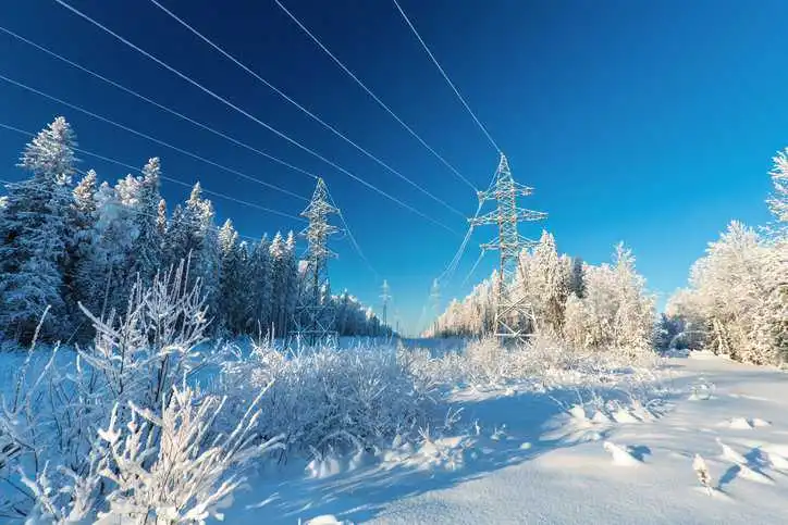 Electrical wires of overhead power line or electrical transmission line covered by snow in the winter forest adhering to IEC 60652:2021.